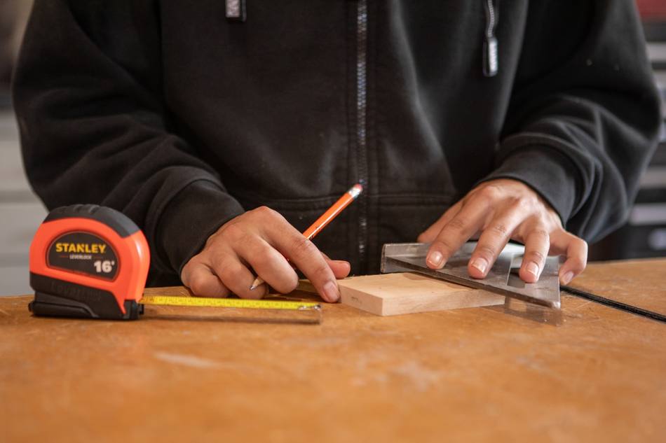 Des mains tracent un repère sur du bois, à l'équerre et au crayon