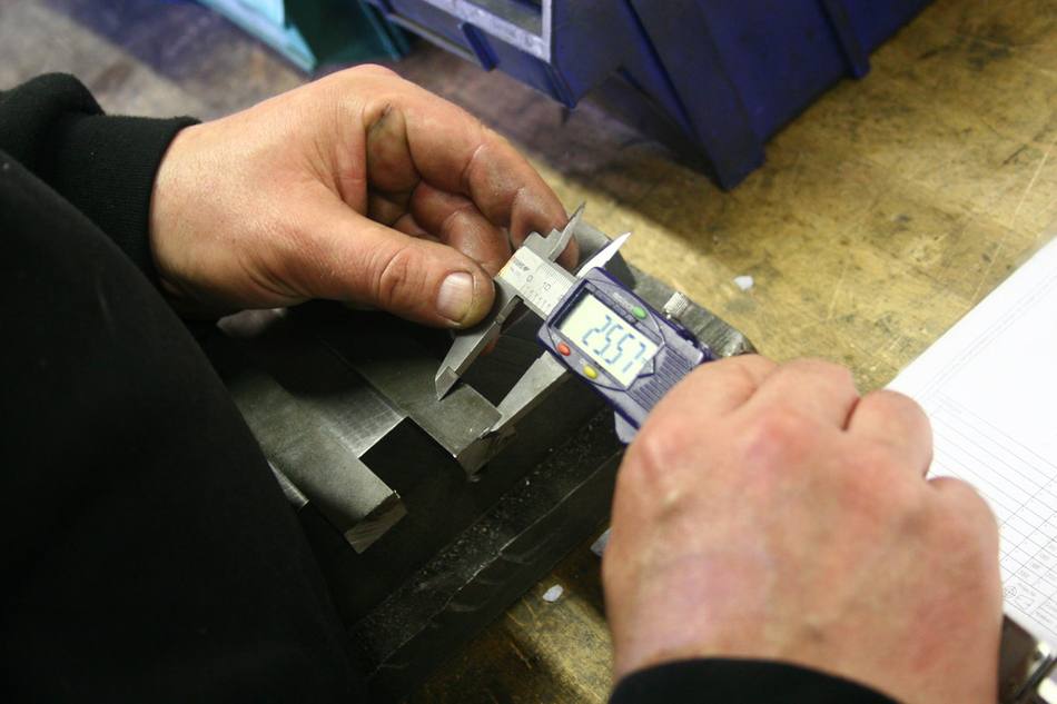Deux mains mesurent une pièce métallique au pied à coulisse